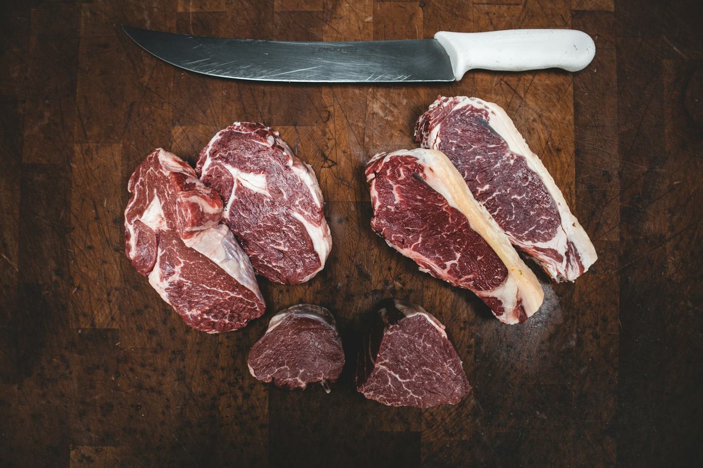 Fresh cuts of beef on a butcher's block beside a knife