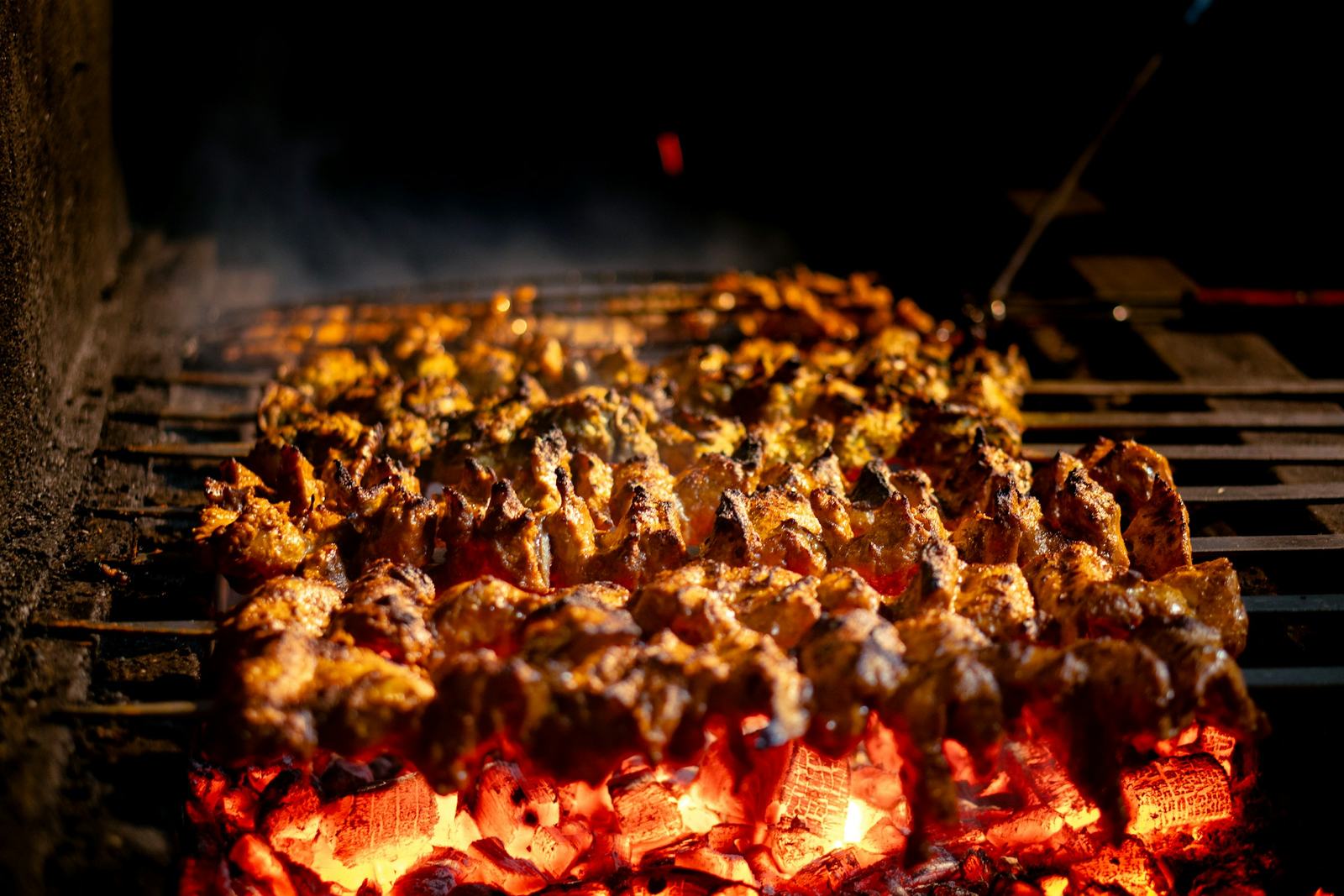 Skewers of kabob grilling over glowing charcoal